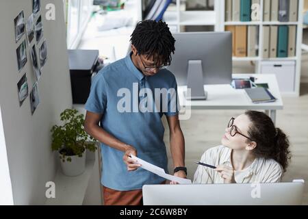 Ritratto ad angolo di due giovani creativi che riesaminano le immagini mentre lavorano all'editing e alla pubblicazione in un ufficio moderno, spazio di copia Foto Stock