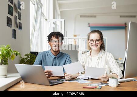 Ritratto di due giovani creativi sorridenti alla fotocamera mentre si rivede le fotografie in ufficio editoriale, copia spazio Foto Stock