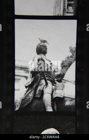 Bella fotografia in bianco e nero d'epoca degli anni '70 di una statua di un uomo seduto su un cavallo mentre tiene un rotolo e un piccione seduto sulla sua testa. Foto Stock