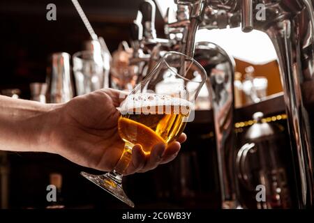 Servizio clienti al bar. Il barman versa una birra dal rubinetto in vetro all'interno Foto Stock