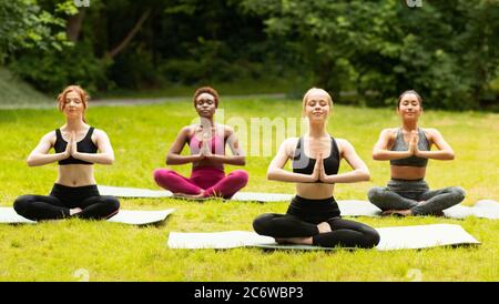 Ragazze multinazionali in abiti sportivi che fanno meditazione yoga su erba fresca al parco Foto Stock