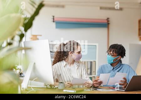 Vista frontale ritratto di due giovani fotografi che indossano maschere mentre si rivedono le foto alla scrivania in studio ufficio, spazio copia Foto Stock