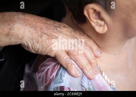 Primo piano delle mani dell'anziano massaggiando delicatamente le spalle della moglie Foto Stock