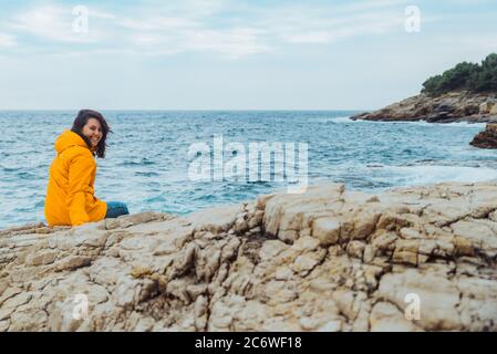 La donna posa sul bordo della scogliera alla ricerca sulle grandi onde Foto Stock