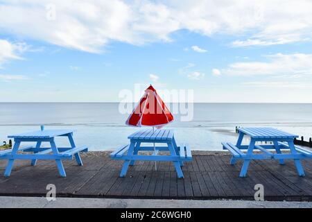 Tavoli e sedie blu luminoso con ombrellone rosso che si affaccia sul mare in estate. Vuoto in attesa di essere riempito di persone Foto Stock