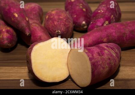 Due metà di una patata dolce tagliata di fronte a patate dolci intere Foto Stock