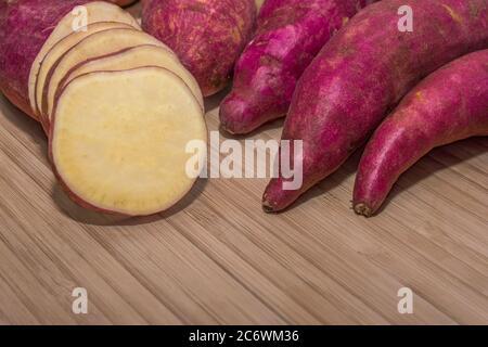Alcune patate dolci tagliate a fette e intere su una superficie di bambù Foto Stock