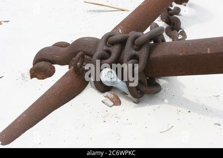 Catena arrugginita avvolta intorno al gambo dell'ancora sulla spiaggia di sabbia bianca Foto Stock