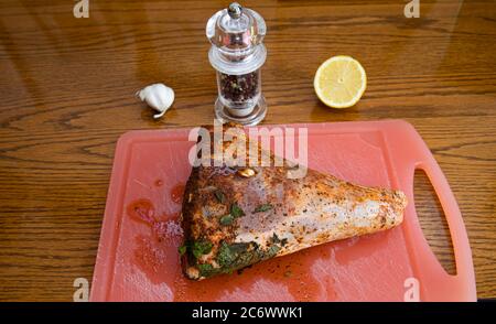 Gamba arrosto marinata di agnello su un tagliere arancione pronto per essere cucinato. Foto Stock