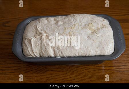 Impasto di pane di fattoria con semi di sesamo in una latta di pane pronta per essere cotta in forno su un tavolo di legno Foto Stock