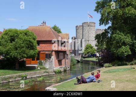 Giovani uomini che si trovano vicino al fiume Stour in una giornata di sole nei giardini Westgate a Canterbury. Foto Stock