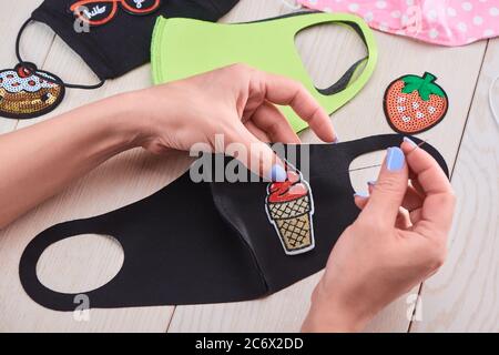 Donna cucire un gelato ricamato cerotto a una maschera nera viso Foto Stock