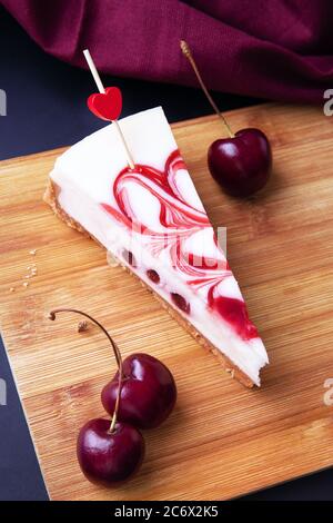 Una fetta di torta fatta in casa con panna bianca e ripieno di ciliegie. Torte fatte in casa con frutti di bosco estivi freschi ciliegia su un tavolo di legno. Fatti in casa Foto Stock