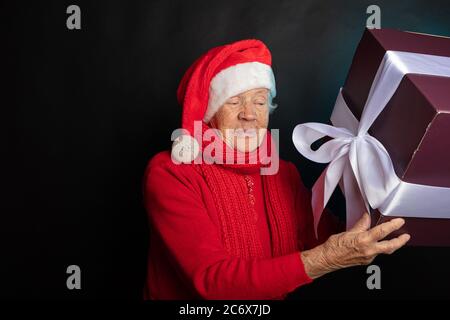 Sly, nonna felice in un cappello gnome sta tenendo un regalo di Capodanno. Su uno sfondo nero studio fotografico. Felice anno nuovo 2021. Foto di alta qualità Foto Stock