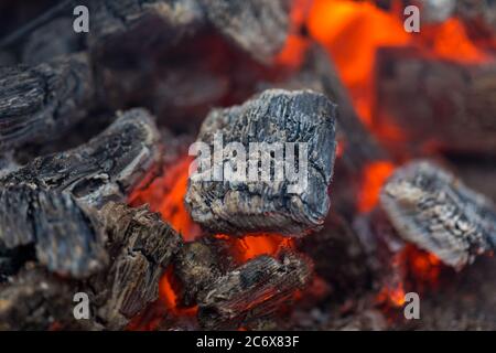 La fiamma incenerisce la legna da ardere e la trasforma in cenere, primo piano, profondità di campo poco profonda. Sfolgitiamo in una stufa grande. Natura struttura di fuoco. La fiamma di Foto Stock