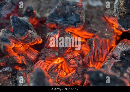 La fiamma incenerisce la legna da ardere e la trasforma in cenere, primo piano, profondità di campo poco profonda. Sfolgitiamo in una stufa grande. Natura struttura di fuoco. La fiamma di Foto Stock