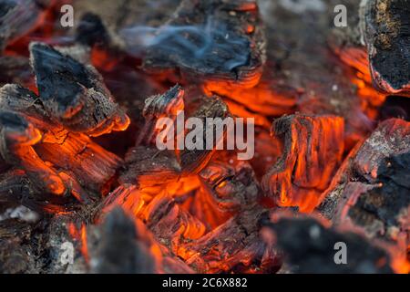 La fiamma incenerisce la legna da ardere e la trasforma in cenere, primo piano, profondità di campo poco profonda. Sfolgitiamo in una stufa grande. Natura struttura di fuoco. La fiamma di Foto Stock