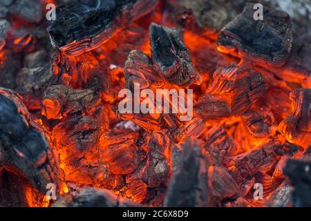 La fiamma incenerisce la legna da ardere e la trasforma in cenere, primo piano, profondità di campo poco profonda. Sfolgitiamo in una stufa grande. Natura struttura di fuoco. La fiamma di Foto Stock