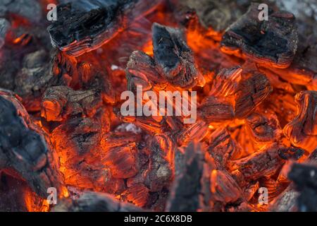 La fiamma incenerisce la legna da ardere e la trasforma in cenere, primo piano, profondità di campo poco profonda. Sfolgitiamo in una stufa grande. Natura struttura di fuoco. La fiamma di Foto Stock