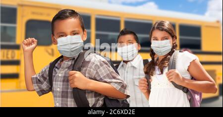 Studenti ispanici vicino a School Bus che indossano maschere facciali. Foto Stock