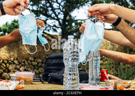 Diverse mani che tengono maschere in picnic con acqua e soda. Concetto di picnic nella nuova normalità, Covid 19. Foto Stock
