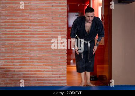 Uomo Karate in posa con un arco per accedere al tatami con kimono nero Foto Stock