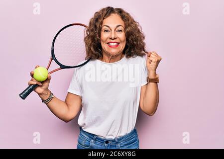 Media età bella sportivo che gioca a tennis tenendo racchetta e palla su sfondo bianco urlando orgoglioso, celebrando la vittoria e il successo molto ex Foto Stock