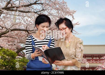Donna anziana che legge una guida di viaggio con sua figlia Foto Stock