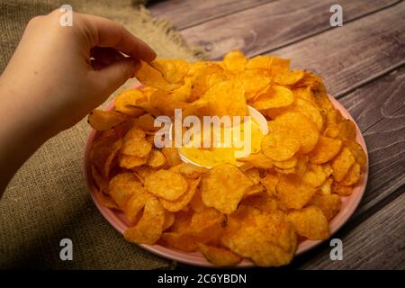 La ragazza prende un chip da un piatto rotondo con patatine e una pentola con salsa di formaggio al centro del piatto. Primo piano Foto Stock