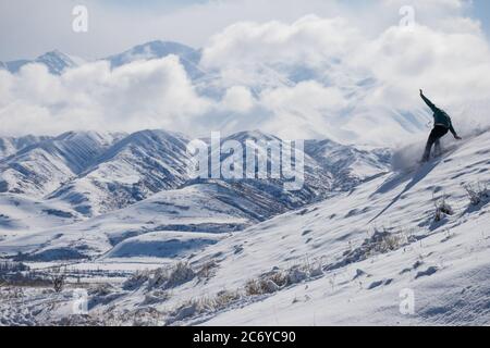 Un snowboarder solista si snoderà lungo una collina nel Chuy Oblast del Kirghizistan durante un tour invernale. Foto Stock