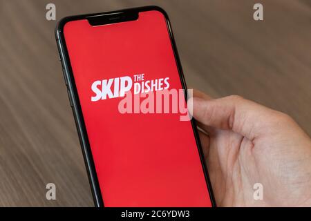 Persona che usa un cellulare con il logo Skip the Dishes, il popolare servizio online di ordinazione e consegna di cibo su schermo. Foto Stock