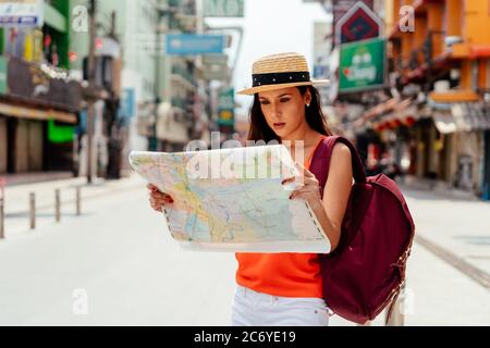 Donna giovane e seria di bruna ispanica che tiene la mappa in strada in vacanza con lo zaino Foto Stock