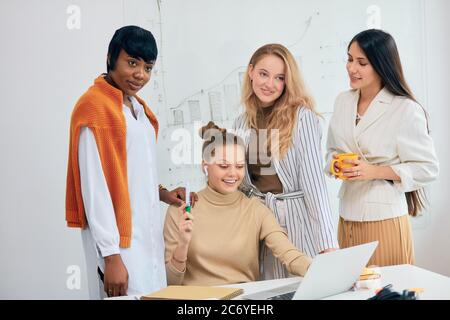 Donne caucasiche e africane, le donne di affari si sono riunite in un moderno ufficio bianco per discutere le idee di affari usando il laptop, lavoro di squadra di belle Signore indossare Foto Stock
