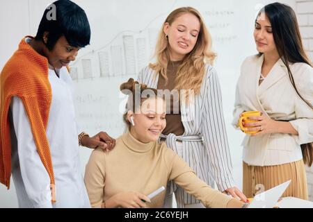 Donne caucasiche e africane, le donne di affari si sono riunite in un moderno ufficio bianco per discutere le idee di affari usando il laptop, lavoro di squadra di belle Signore indossare Foto Stock