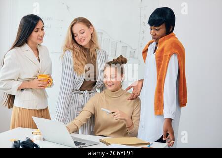 Donne caucasiche e africane, le donne di affari si sono riunite in un moderno ufficio bianco per discutere le idee di affari usando il laptop, lavoro di squadra di belle Signore indossare Foto Stock