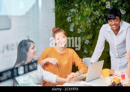 Fidata giovane donna africana in camicia bianca stand parlare con giovani donne caucasiche, insegnare business mentoring, discutere di strategia in ufficio moderno Foto Stock