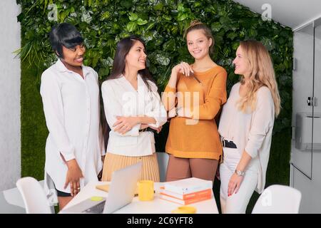 Sorridenti donne entusiaste che si uniscono in un ufficio moderno, guardarsi l'un l'altro e guardare la macchina fotografica Foto Stock