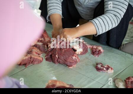 Mani di donne adulte che tengono e affettano carne sacrificale durante la celebrazione di Eid al-Adha Foto Stock