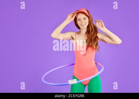 bella ragazza zenzero ben sagomata con lunghi capelli rossi rotolerà hula hoop durante il riscaldamento di esercizio alla classe aerobica, si sente fresco e pieno di energia, wa Foto Stock