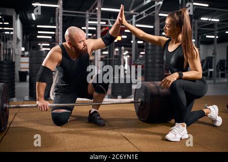 Giovane moglie attiva e marito aggrappano le mani in un gesto di vittoria, guardando via con forte espressione, facendo scommesse, riposandosi in palestra, salute e concetto di sport, dentro Foto Stock