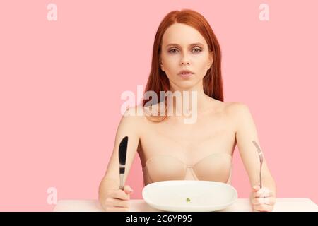 Modello femminile dai capelli rossi, essendo su dieta rigorosa che soffre di anoressia, ossessionato da undereating, paura di sovrappeso. Studio isolato girato su rosa b Foto Stock