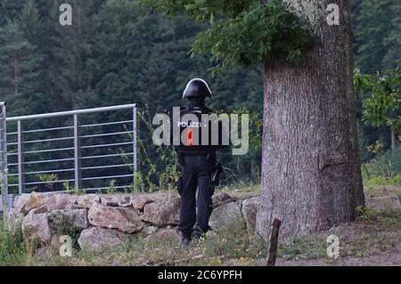 Oppenau, Germania. 13 luglio 2020. Un poliziotto si trova di fronte ad una zona boscosa su una strada vicino a Oppenau. Il giorno prima, un uomo aveva minacciato e disarmato gli ufficiali di polizia durante un'ispezione. Poi fuggì. Un grande contingente sta cercando il fuggitivo. Credit: Sven Kohls/SDMG/dpa/Alamy Live News Foto Stock