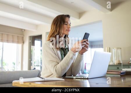 Donna con un computer portatile che utilizza uno smartphone a casa Foto Stock