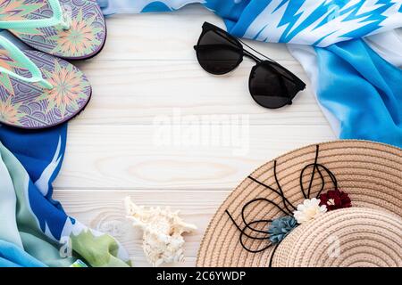 Accessori per la spiaggia estiva. Infradito colorato, guscio, occhiali da sole neri, pareo blu e cappello di paglia su sfondo di legno. Il concetto di vacanza mare, le Foto Stock