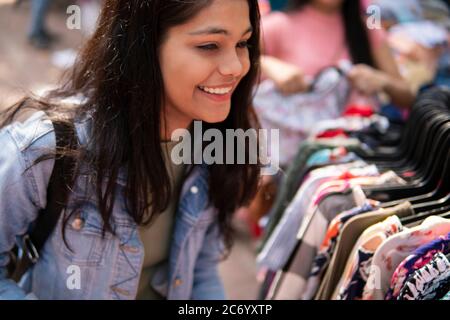 Felice ragazza teen in ritardo cercando e acquistare vestiti dal mercato di strada all'aperto di Delhi, India al giorno. Sparare luogo Sarojini Nagar, Delhi, India. Foto Stock