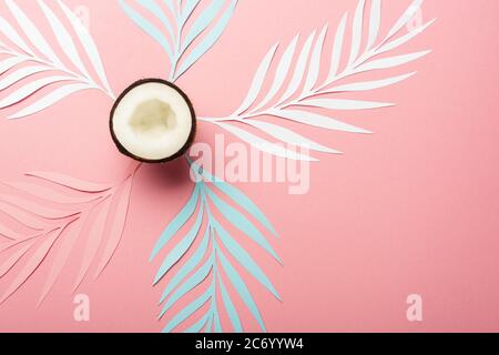 vista dall'alto di foglie di palma tagliate di carta bianca, rosa e blu e metà di cocco su sfondo rosa Foto Stock