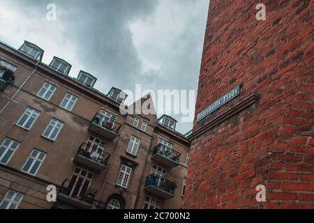 Vista ad angolo basso del cartello con il nome della strada sulla facciata in mattoni dell'edificio e cielo nuvoloso sullo sfondo a Copenhagen, Danimarca Foto Stock