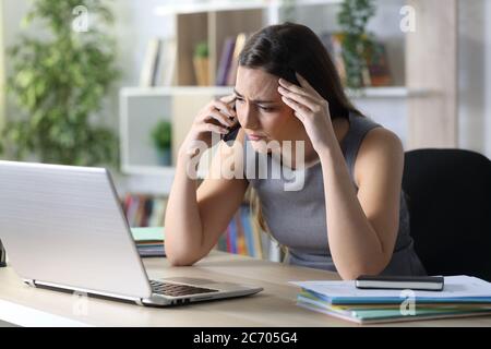Donna imprenditore preoccupata chiama su smartphone con un computer portatile seduto su una scrivania a casa Foto Stock