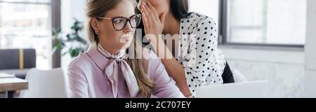 intestazione di sito web di donna d'affari che sussurra in orecchio di collaboratore in occhiali mentre gossiping in ufficio Foto Stock
