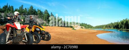 Quad ATV guida persone. Felice coppia sorridente ciclisti sulla spiaggia presso il bellissimo lago. Foy, lago Foyross, Sudbury, Ontario, Canada. Foto Stock